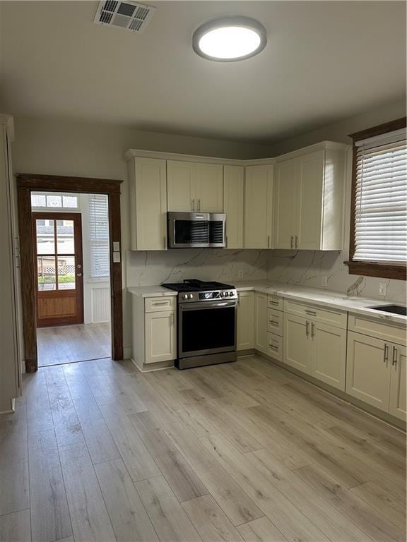 1401 Jefferson St, Gretna, LA 70053 - kitchen with appliances with stainless steel finishes, light countertops, light wood finished floors, tasteful backsplash, and white cabinets