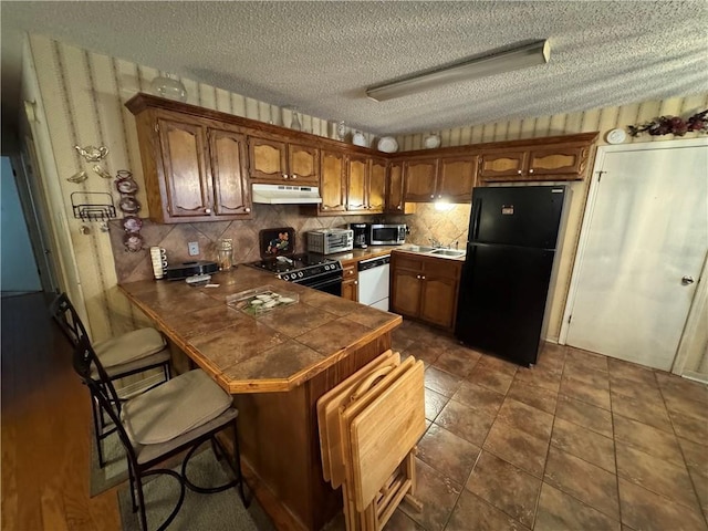 6655 Dalark Dr, Baton Rouge, LA 70812 - kitchen with black appliances, under cabinet range hood, a peninsula, a textured ceiling, and backsplash