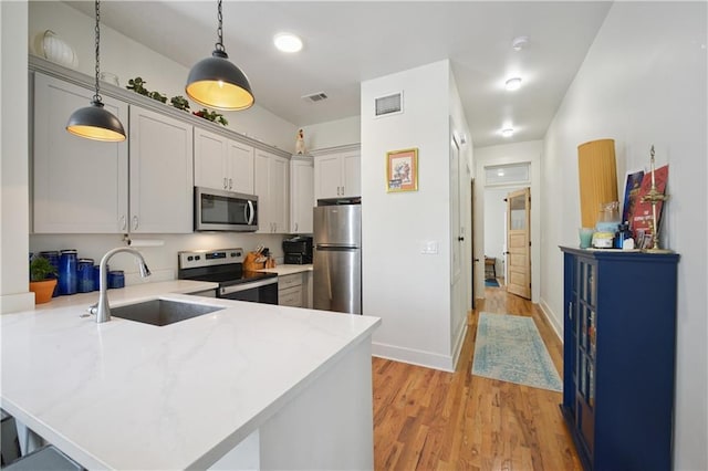 20810 S Scott St, New Orleans, LA 70119 - kitchen featuring appliances with stainless steel finishes, a peninsula, pendant lighting, light wood-style flooring, and a kitchen breakfast bar