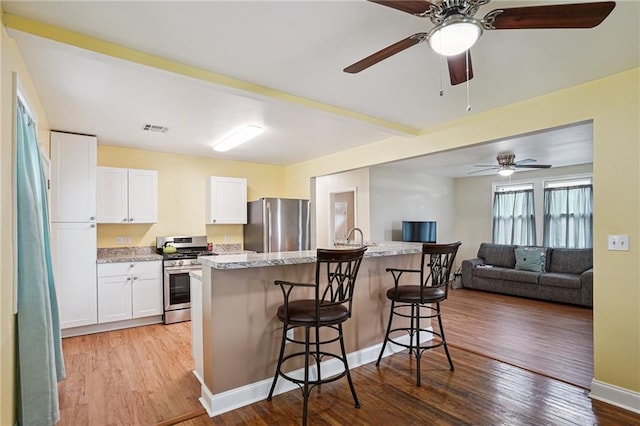 3713 Lausat St, Metairie, LA 70001 - kitchen featuring appliances with stainless steel finishes, wood finished floors, a breakfast bar, white cabinetry, and a ceiling fan