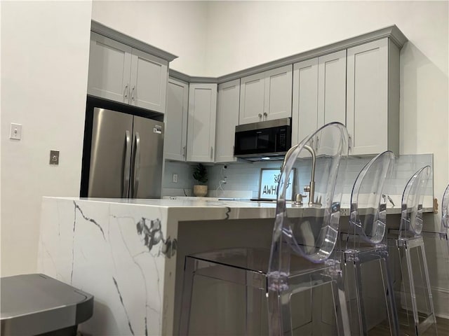 1201 Canal St Unit 216, New Orleans, LA 70112 - kitchen with appliances with stainless steel finishes, gray cabinets, backsplash, a peninsula, and a kitchen bar