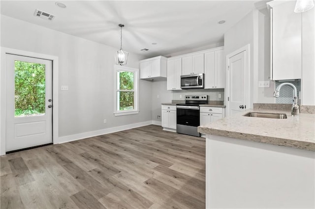 74446 Delta Ave, Covington, LA 70435 - kitchen featuring stainless steel appliances, white cabinets, light stone countertops, light wood-style floors, and decorative light fixtures