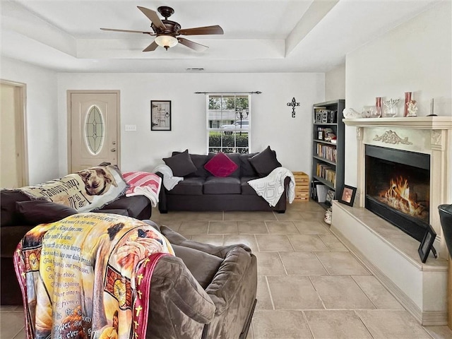 2411 Jay St, Slidell, LA 70460 - living room featuring a tray ceiling, a ceiling fan, a warm lit fireplace, and tile patterned flooring