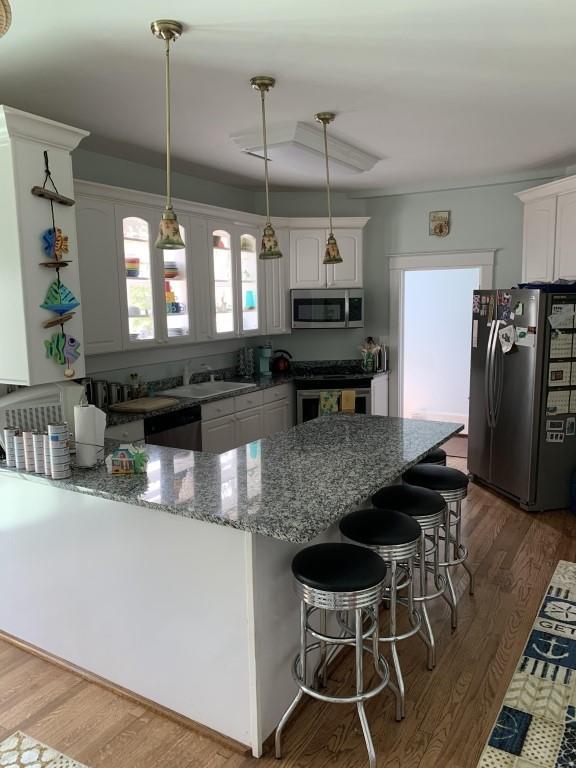 2527 Calhoun St, New Orleans, LA 70118 - kitchen featuring appliances with stainless steel finishes, stone countertops, wood finished floors, white cabinetry, and hanging light fixtures