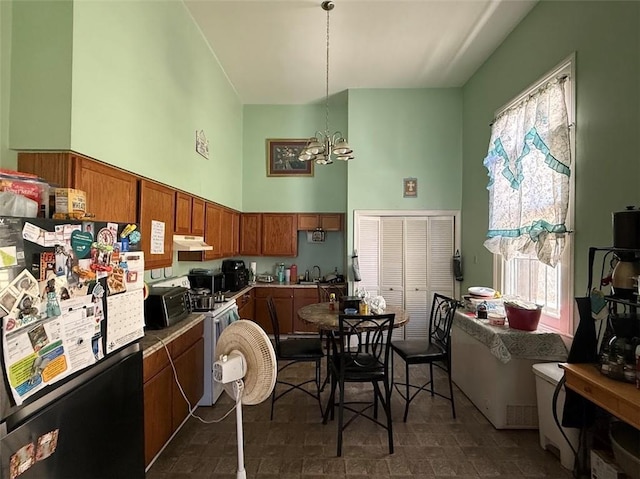 223335 Baronne St, New Orleans, LA 70113 - kitchen with freestanding refrigerator, under cabinet range hood, a chandelier, a high ceiling, and brown cabinets