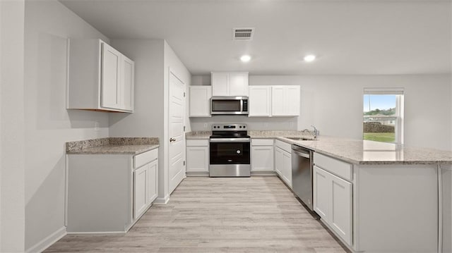 4674 Marais River Dr, Slidell, LA 70461 - kitchen featuring stainless steel appliances, a peninsula, light wood finished floors, light stone countertops, and white cabinetry