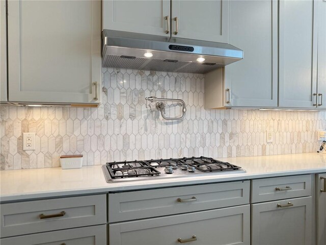 242 Douglas Dr, New Orleans, LA 70123 - kitchen with under cabinet range hood, stainless steel gas stovetop, light countertops, gray cabinetry, and decorative backsplash