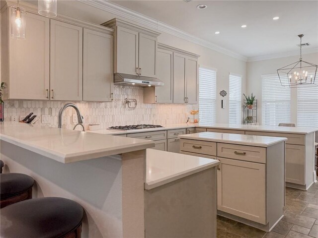 242 Douglas Dr, New Orleans, LA 70123 - kitchen featuring a peninsula, under cabinet range hood, backsplash, crown molding, and light countertops