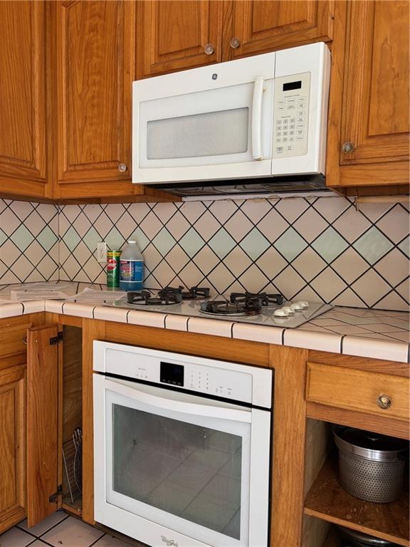 72075 Gum St, Abita Springs, LA 70420 - kitchen with white appliances, decorative backsplash, brown cabinetry, and tile countertops