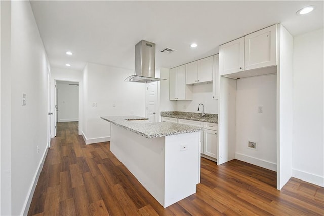 3304 Metropolitan St, New Orleans, LA 70126 - kitchen with island range hood, white cabinetry, light stone counters, dark wood finished floors, and recessed lighting