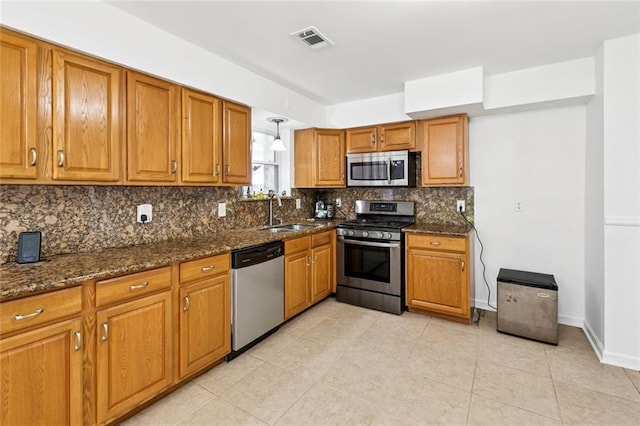 3809 N Woodlawn Ave, Metairie, LA 70006 - kitchen featuring stainless steel appliances, brown cabinets, decorative backsplash, dark stone counters, and light tile patterned flooring