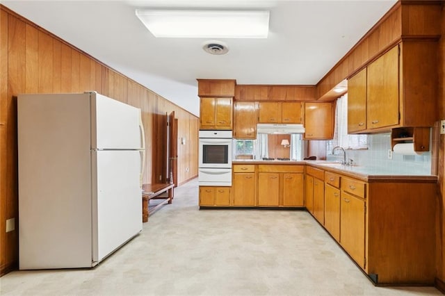 2209 Athania Pkwy, Metairie, LA 70001 - kitchen with white appliances, a warming drawer, brown cabinets, wooden walls, and under cabinet range hood