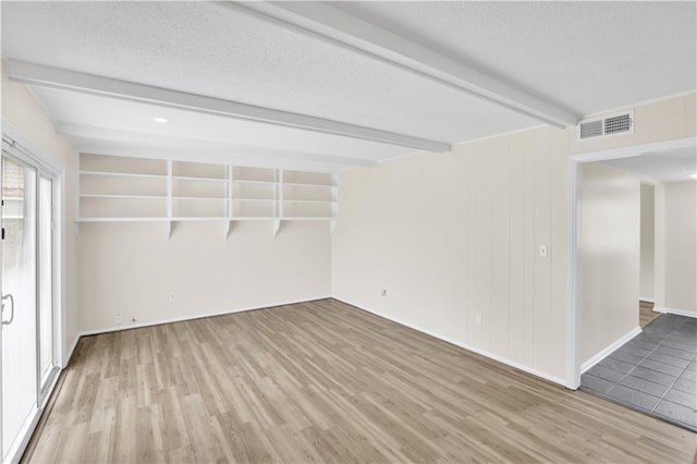 unfurnished room featuring beamed ceiling, wood finished floors, and a textured ceiling