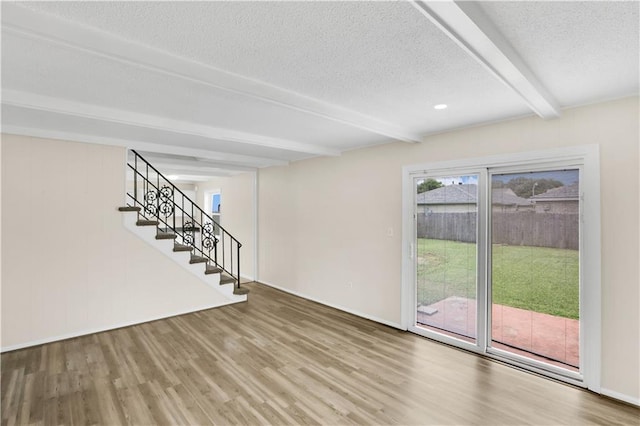 unfurnished living room with beamed ceiling, wood finished floors, a textured ceiling, and stairway