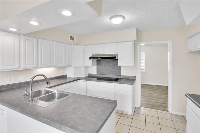 kitchen featuring under cabinet range hood, white cabinetry, light tile patterned floors, a peninsula, and a textured ceiling