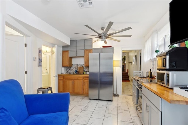 1801 Adams St, New Orleans, LA 70118 - kitchen featuring appliances with stainless steel finishes, light marble finish floors, butcher block countertops, a ceiling fan, and tasteful backsplash