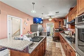 2936 General Ogden St, New Orleans, LA 70118 - kitchen with a kitchen island, brown cabinetry, ceiling fan, appliances with stainless steel finishes, and decorative light fixtures