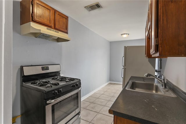 71315 Radiance St, Metairie, LA 70001 - kitchen featuring stainless steel range with gas stovetop, under cabinet range hood, dark countertops, light tile patterned flooring, and brown cabinetry