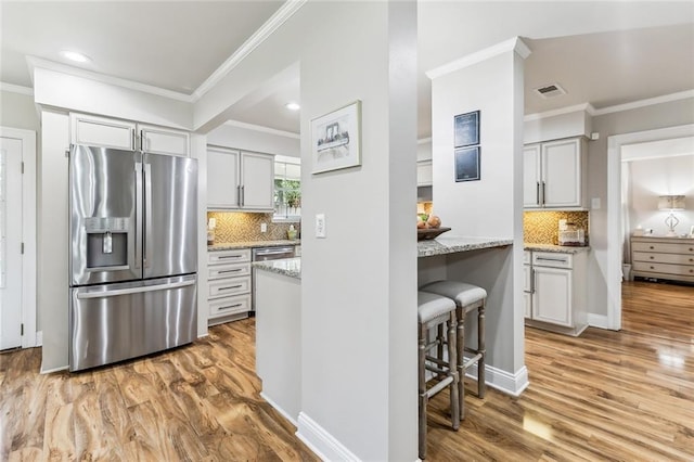 163 Tchefuncte Dr, Covington, LA 70433 - kitchen featuring appliances with stainless steel finishes, ornamental molding, light wood-style floors, decorative backsplash, and light stone countertops