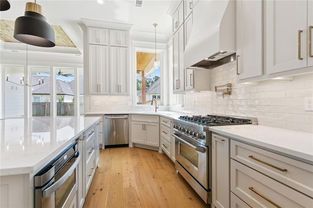 4233 Cypress Point Dr, Covington, LA 70433 - kitchen featuring stainless steel appliances, premium range hood, light wood-style floors, backsplash, and pendant lighting