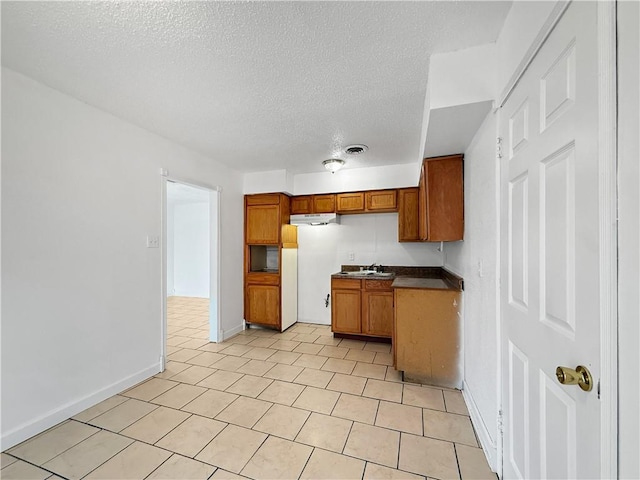 1024 Marshall Dr, Marrero, LA 70072 - kitchen featuring brown cabinetry, under cabinet range hood, a textured ceiling, dark countertops, and light tile patterned floors