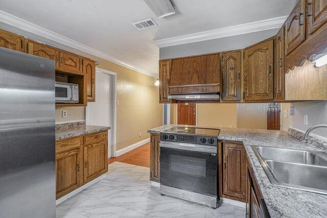 1832 Faith Pl, Gretna, LA 70056 - kitchen featuring appliances with stainless steel finishes, light marble finish flooring, ornamental molding, under cabinet range hood, and brown cabinetry