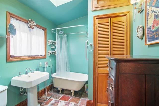 91315 Arabella St, New Orleans, LA 70115 - bathroom featuring lofted ceiling, a freestanding bath, a skylight, a shower with shower curtain, and stone finish floors