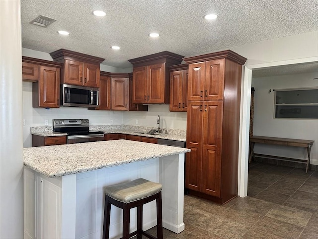 624 Taylorbrook St, Gretna, LA 70053 - kitchen featuring appliances with stainless steel finishes, a textured ceiling, a breakfast bar area, light stone counters, and recessed lighting