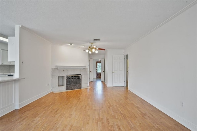4152 Cognac Dr, Kenner, LA 70065 - unfurnished living room with ceiling fan, light wood-style flooring, ornamental molding, a tiled fireplace, and a textured ceiling