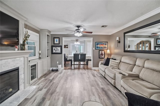 4969 Tasha Ln, Jean Lafitte, LA 70067 - living room featuring a ceiling fan, a textured ceiling, light wood-type flooring, crown molding, and a fireplace