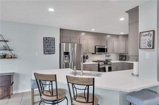 497 Jj Ln, Covington, LA 70433 - kitchen featuring stainless steel appliances, gray cabinets, a kitchen breakfast bar, tasteful backsplash, and light countertops
