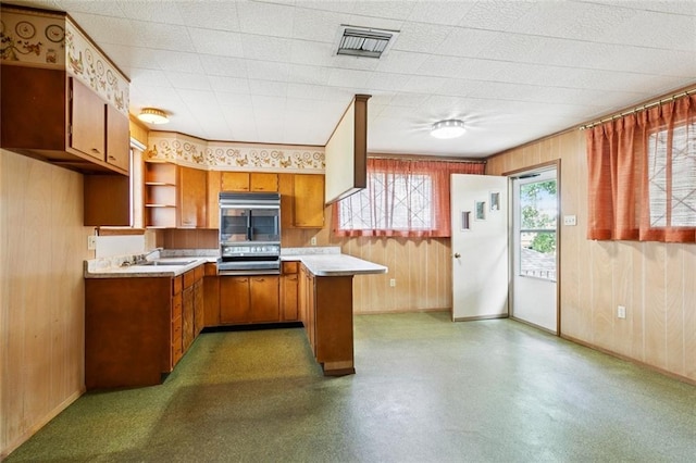 953 Homestead Ave, Metairie, LA 70005 - kitchen with brown cabinetry, light countertops, wooden walls, a peninsula, and wall oven