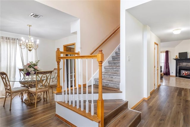 638 Colony Park Dr, La Place, LA 70068 - staircase featuring wood finished floors, a chandelier, healthy amount of natural light, and a warm lit fireplace