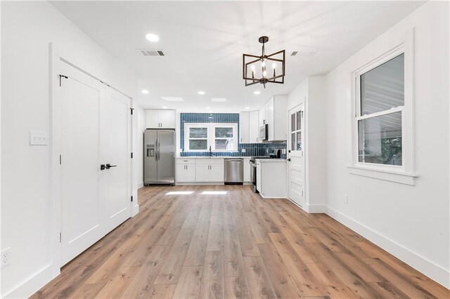 566 Gelpi Ave, Jefferson, LA 70121 - kitchen featuring stainless steel appliances, white cabinets, light wood finished floors, a chandelier, and backsplash