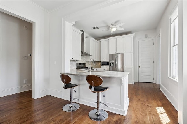 5540 Pitt St, New Orleans, LA 70115 - kitchen featuring stainless steel appliances, wall chimney range hood, a peninsula, white cabinets, and a ceiling fan