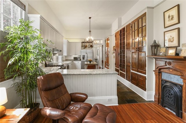 401 Pelican Ave, New Orleans, LA 70114 - kitchen with stone tile flooring, stainless steel fridge, a chandelier, a peninsula, and light stone counters