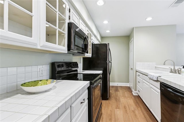 3523 Audubon Trce Unit 3523, Jefferson, LA 70121 - kitchen featuring black appliances, tile counters, white cabinets, light wood-type flooring, and glass insert cabinets