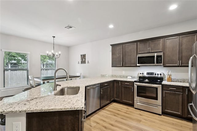 41763 Whisper Woods Rd, Ponchatoula, LA 70454 - kitchen featuring appliances with stainless steel finishes, a peninsula, dark brown cabinets, light wood finished floors, and a chandelier