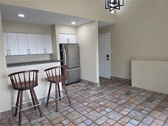 4829 Wabash St Unit 307, Metairie, LA 70001 - kitchen with freestanding refrigerator, a kitchen breakfast bar, white cabinetry, light stone finish flooring, and dark countertops