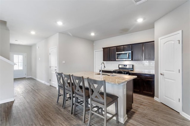 7542 1ST Lake Dr, Slidell, LA 70461 - kitchen with stainless steel appliances, a center island with sink, a kitchen bar, dark wood-style flooring, and light stone countertops