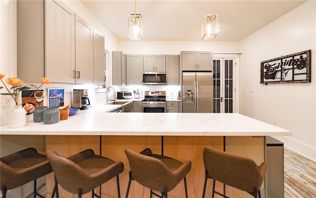 623-25 Louisa St, New Orleans, LA 70117 - kitchen featuring appliances with stainless steel finishes, a peninsula, gray cabinets, a kitchen breakfast bar, and light stone countertops
