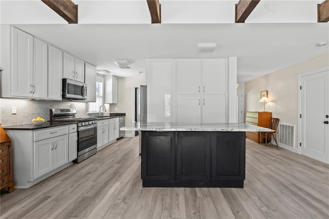 59246 Cypress Bayou Ln, Lacombe, LA 70445 - kitchen with appliances with stainless steel finishes, light wood finished floors, white cabinets, beam ceiling, and a kitchen island