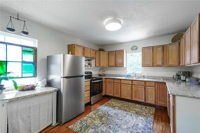 2816 Berwick St, Jefferson, LA 70121 - kitchen featuring appliances with stainless steel finishes, a textured ceiling, dark wood finished floors, brown cabinets, and light stone countertops