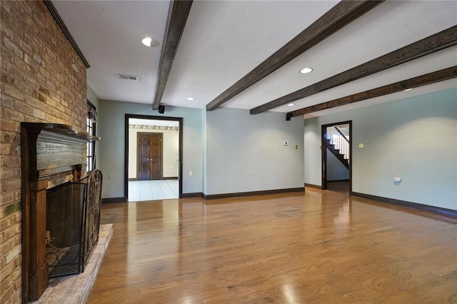 3541 Alan St, Metairie, LA 70002 - unfurnished living room with light wood-style flooring, beam ceiling, a textured ceiling, a fireplace, and stairs