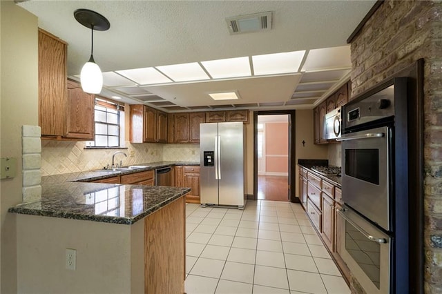 3541 Alan St, Metairie, LA 70002 - kitchen featuring stainless steel appliances, a peninsula, tasteful backsplash, hanging light fixtures, and brown cabinetry