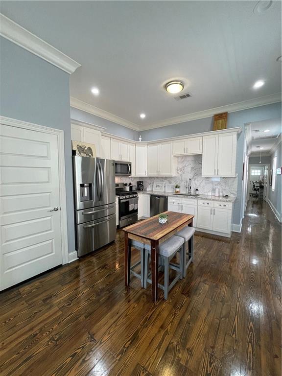 2272 N Robertson St, New Orleans, LA 70117 - kitchen featuring appliances with stainless steel finishes, dark wood-type flooring, white cabinets, ornamental molding, and backsplash