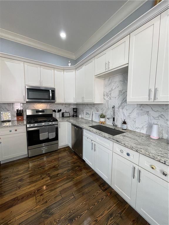2272 N Robertson St, New Orleans, LA 70117 - kitchen featuring appliances with stainless steel finishes, ornamental molding, dark wood finished floors, white cabinets, and light stone counters