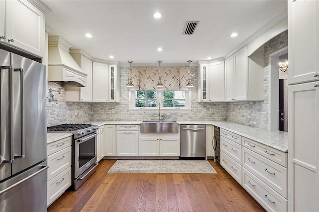 9 Hennessey Ct, River Ridge, LA 70123 - kitchen featuring appliances with stainless steel finishes, premium range hood, glass insert cabinets, tasteful backsplash, and white cabinets