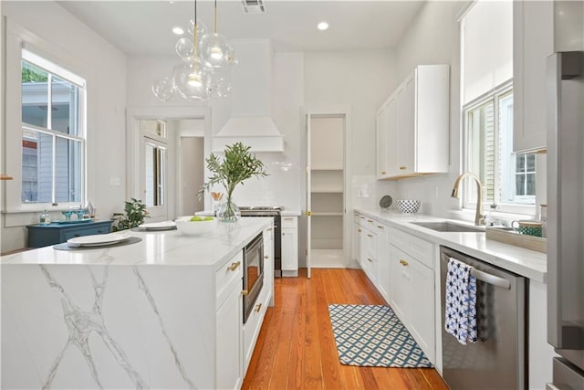 3311 Saint Ann St, New Orleans, LA 70119 - kitchen featuring stainless steel appliances, white cabinets, light wood-type flooring, a kitchen island, and hanging light fixtures
