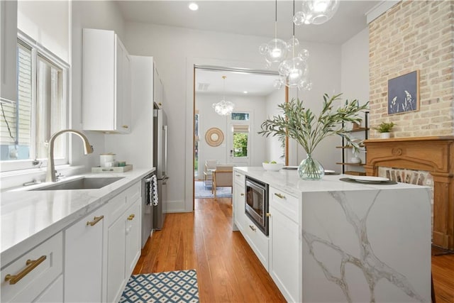 3311 Saint Ann St, New Orleans, LA 70119 - kitchen with appliances with stainless steel finishes, white cabinetry, light wood-type flooring, a kitchen island, and a chandelier